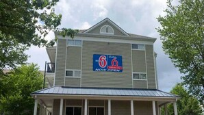 Un motel de dos pisos con un logotipo '6', un porche cubierto y un letrero que dice 'ABIERTO'.