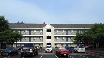 A multi-story hotel with a central entrance, parking lot, and a clear sky.