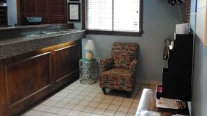 Una cocina pequeña con suelo de baldosas, una encimera de madera, un sillón estampado, una mesita con lámpara y un televisor montado en la pared.