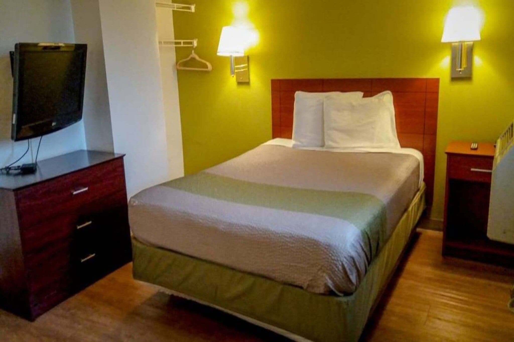A hotel room with a bed, bedside tables, a TV, and wall-mounted lamps.