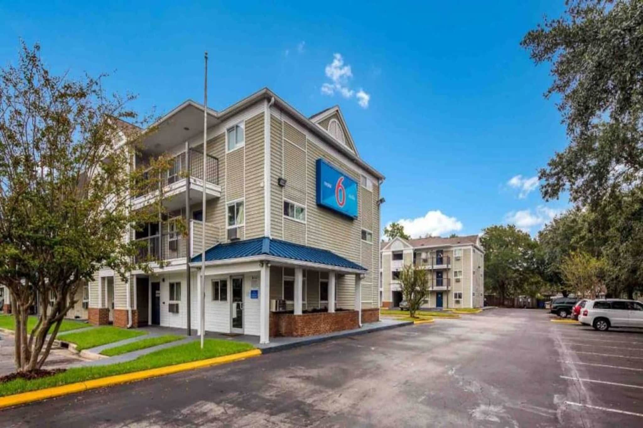 A multi-story hotel with a prominent '6' sign, a covered entrance, and a parking lot.
