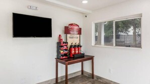 Een kamer met een wandgemonteerde flatscreen televisie, een tafel met koffievoorziening en een raam met uitzicht op bomen.