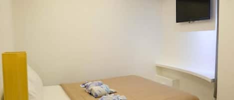 A hotel room with a bed, a television mounted on the wall, and a bedside table.