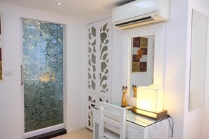 Una habitación con una puerta de cristal satinado, un armario blanco con espejo y una silla blanca.