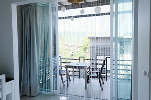 Habitación con puerta de vidrio corredera que da a un balcón exterior con mesa y sillas.