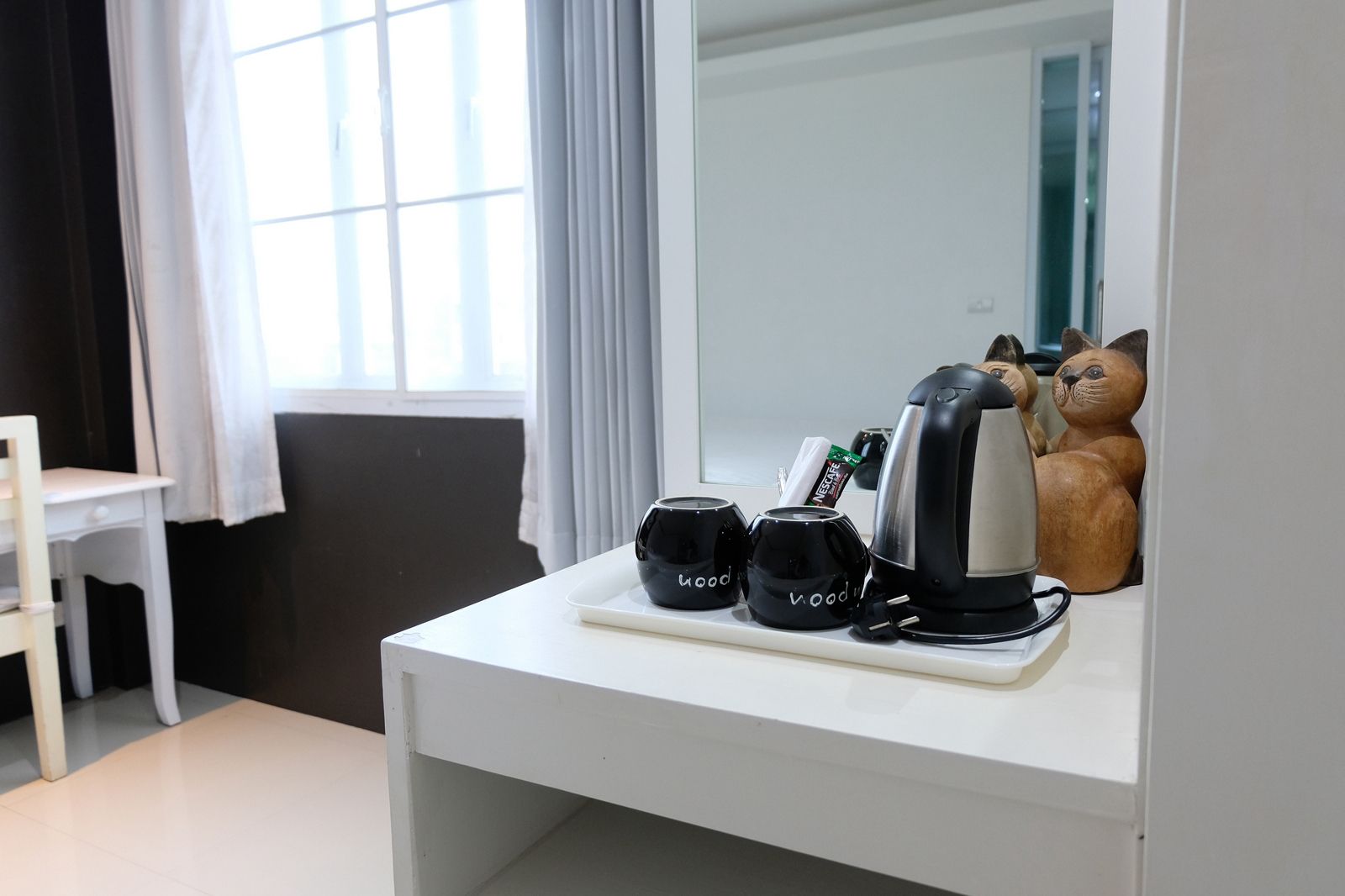 A white desk with a kettle, two black mugs, and a small plant.