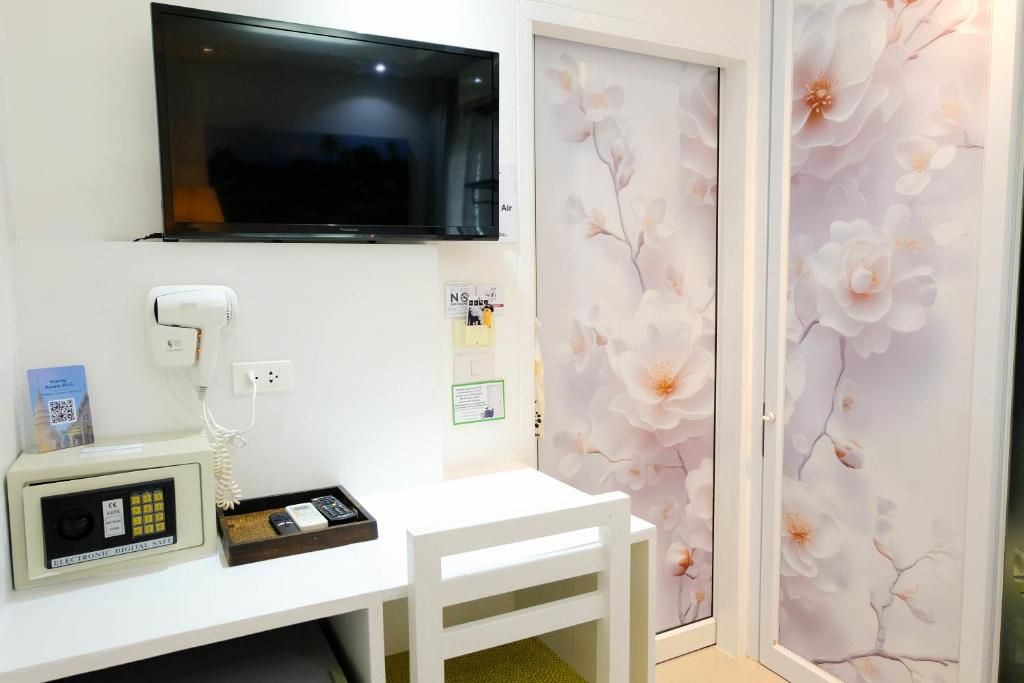 A room with a flat-screen TV mounted on the wall, a telephone with a payphone, and a small table with a tray.