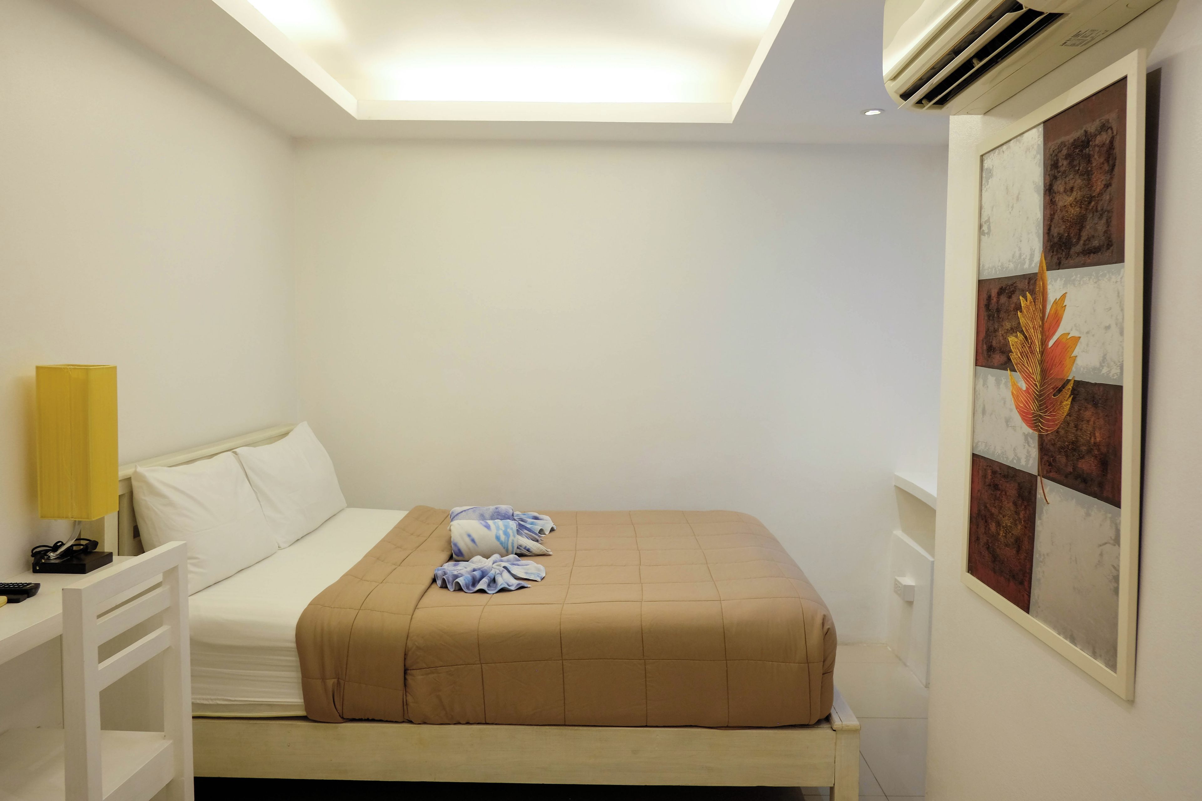 A hotel room with a bed, a bedside table with a lamp, and a wall-mounted artwork.