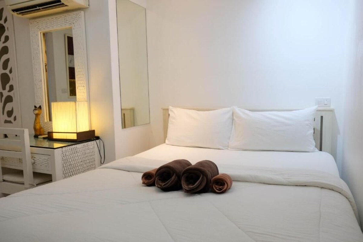Hotellihuone, jossa on sänky, yöpöytä, peili ja sängyllä rullalle taitetut pyyhkeet.