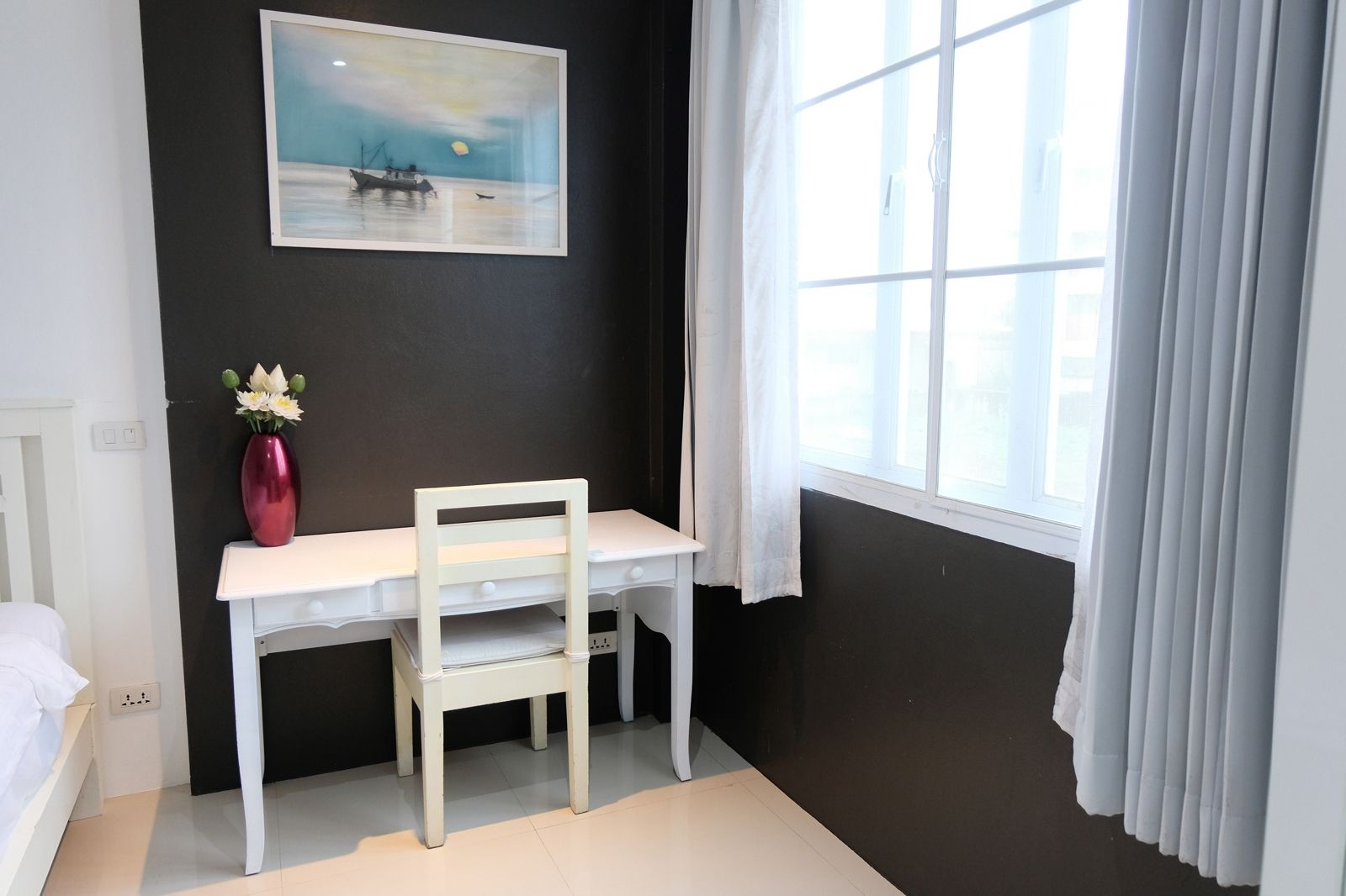Een kamer met een wit bureau, een stoel, een vaas met bloemen, een schilderij aan de muur en een raam met gordijnen.