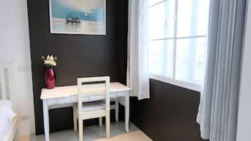 A room with a white desk, a chair, a vase with flowers, a painting on the wall, and a window with curtains.