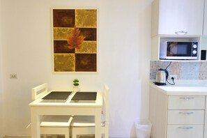 Una kitchenette pequeña con microondas, hervidor y un armario blanco.