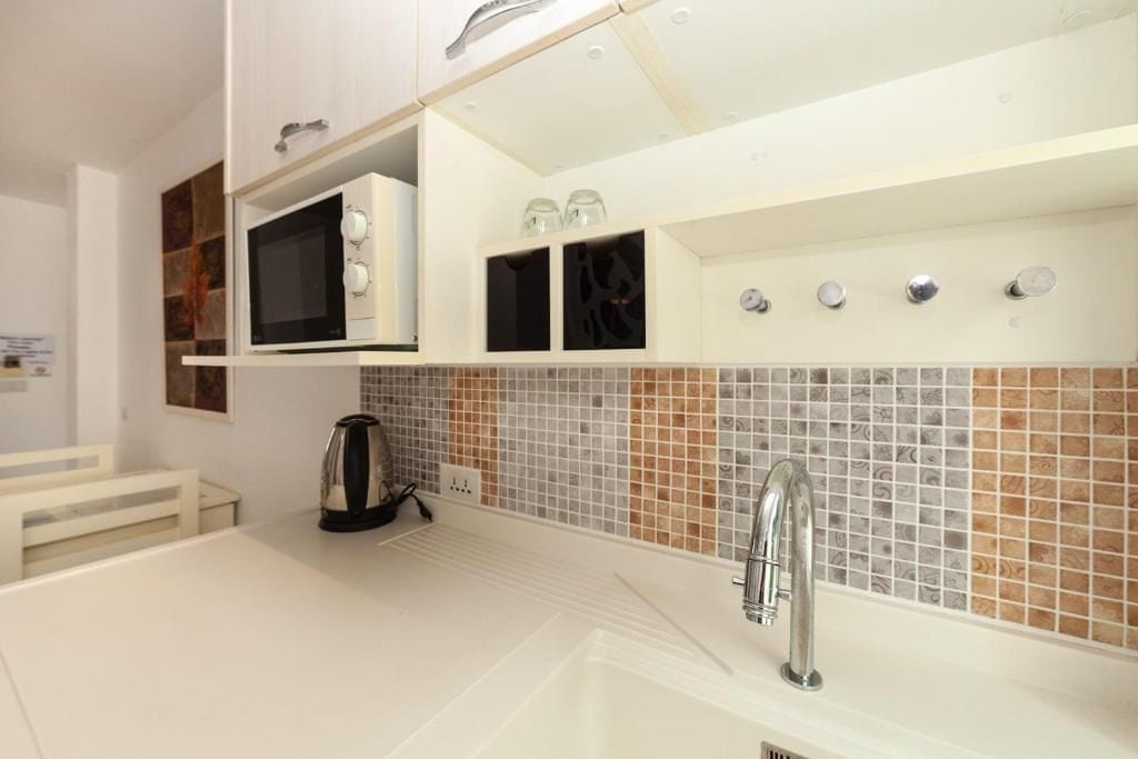 A modern kitchen with a built-in microwave, a kettle, and a sink with a faucet.