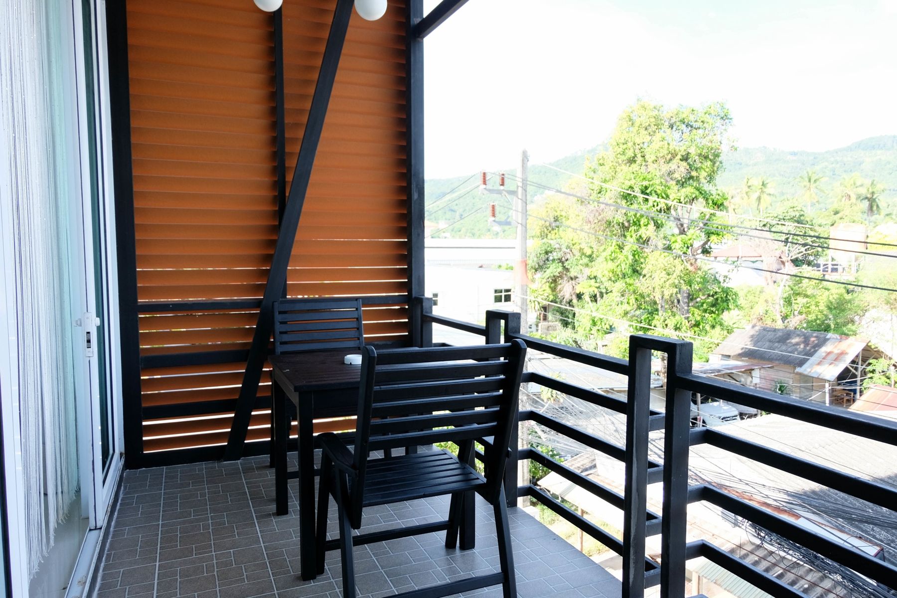 A balcony with two chairs and a table, overlooking a street with buildings and trees.