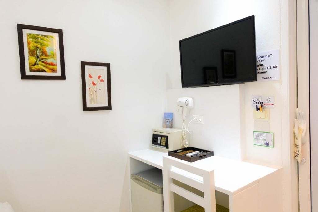 Une chambre d’hôtel avec un bureau blanc, un téléviseur à écran plat fixé au mur, un sèche-cheveux et une petite table avec un plateau.