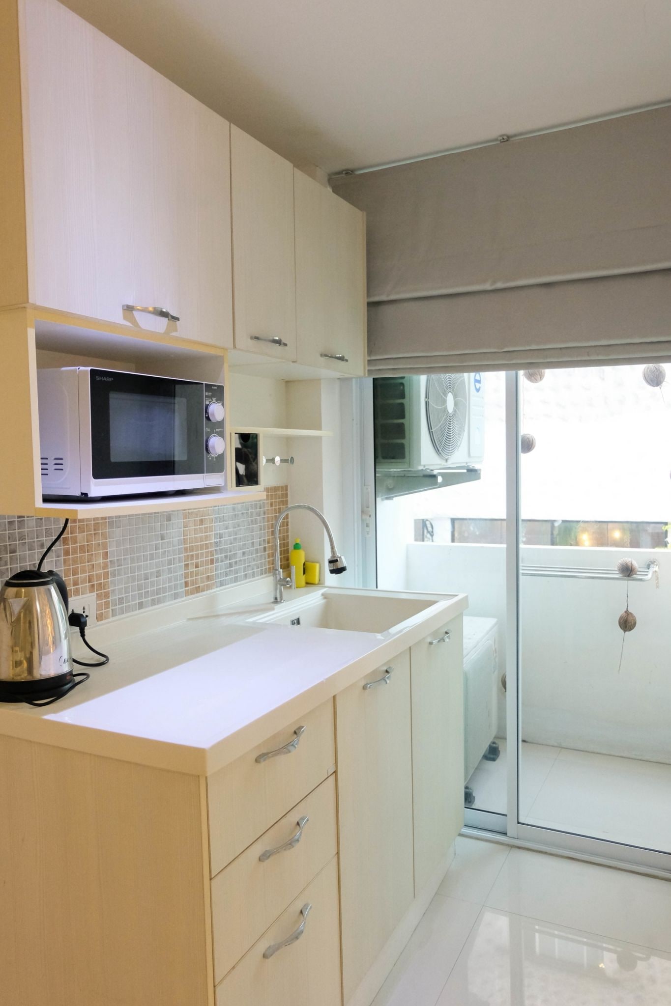 Une cuisine moderne avec des meubles blancs, un four à micro-ondes, une bouilloire et un évier.