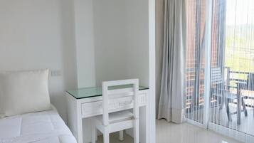 A bedroom with a bed, a white desk, and a chair. There is a window with curtains.