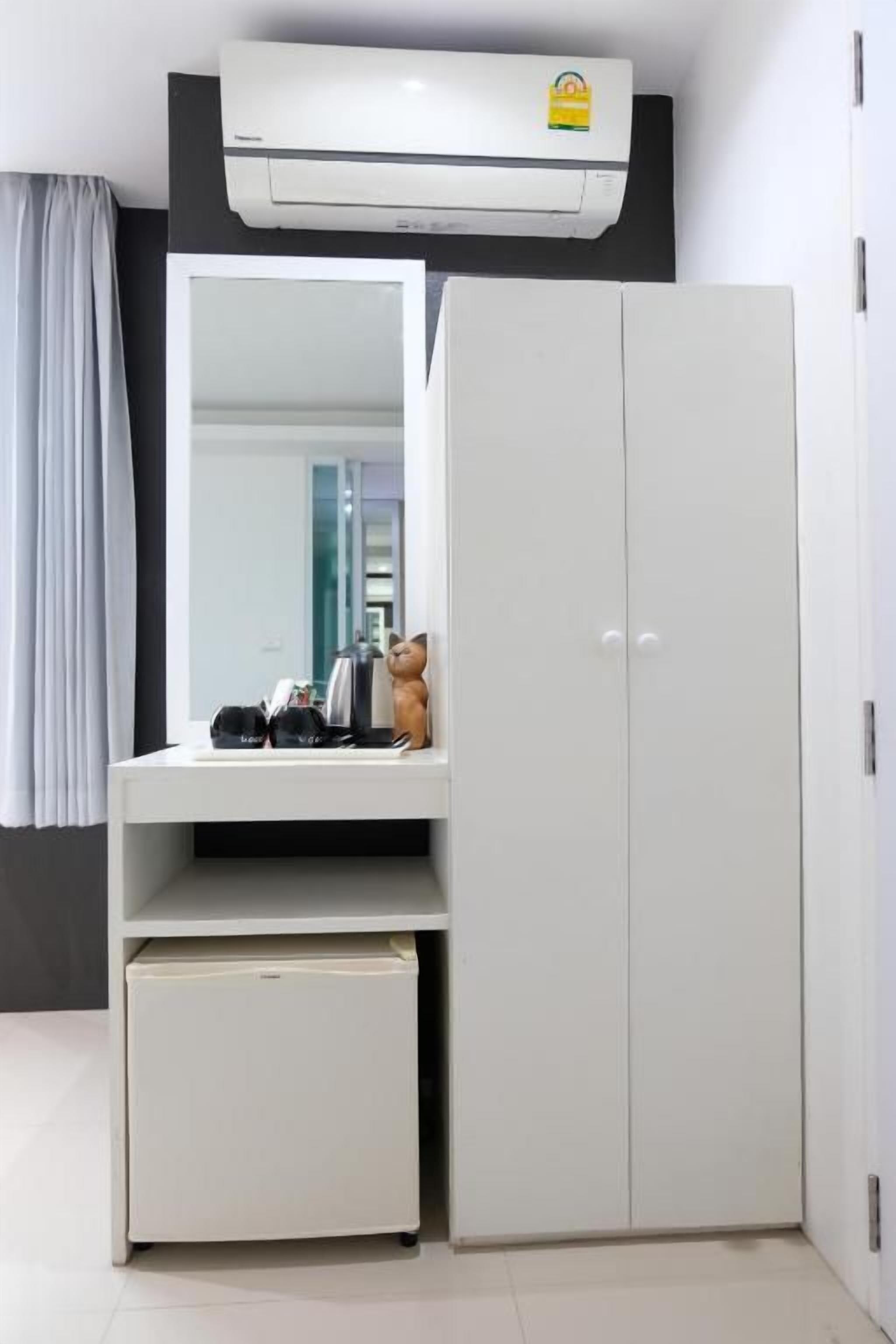 A room with a white wardrobe, a mirror, and a small white cabinet.