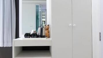 A room with a white wardrobe, a mirror, and a small white cabinet.