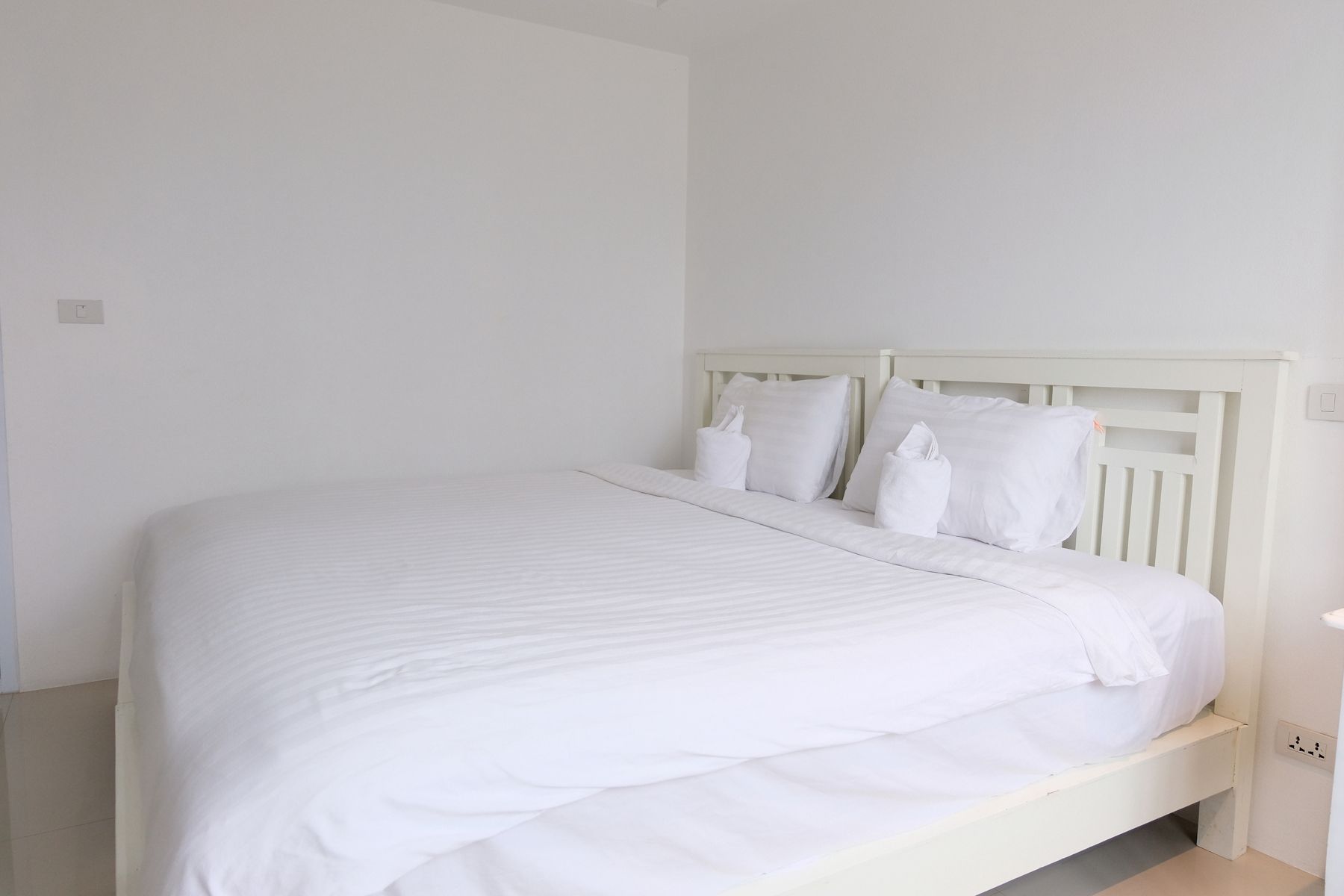 Un lit blanc avec une tête de lit en bois, dans une pièce aux murs blancs.