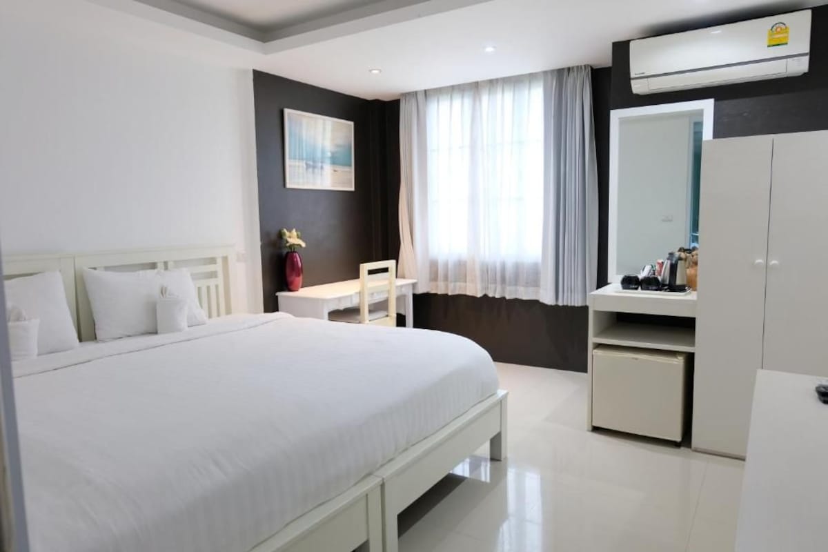 Hotellihuone, jossa on sänky, työpöytä, tuoli, vaatekaappi ja ikkuna, jossa on verhot.