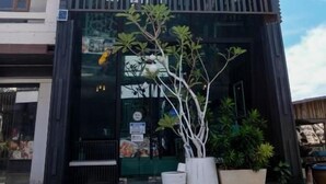 Un edifici amb un rètol que diu 'BAANPOON APARTMENT' i una planta gran en test amb el planter.