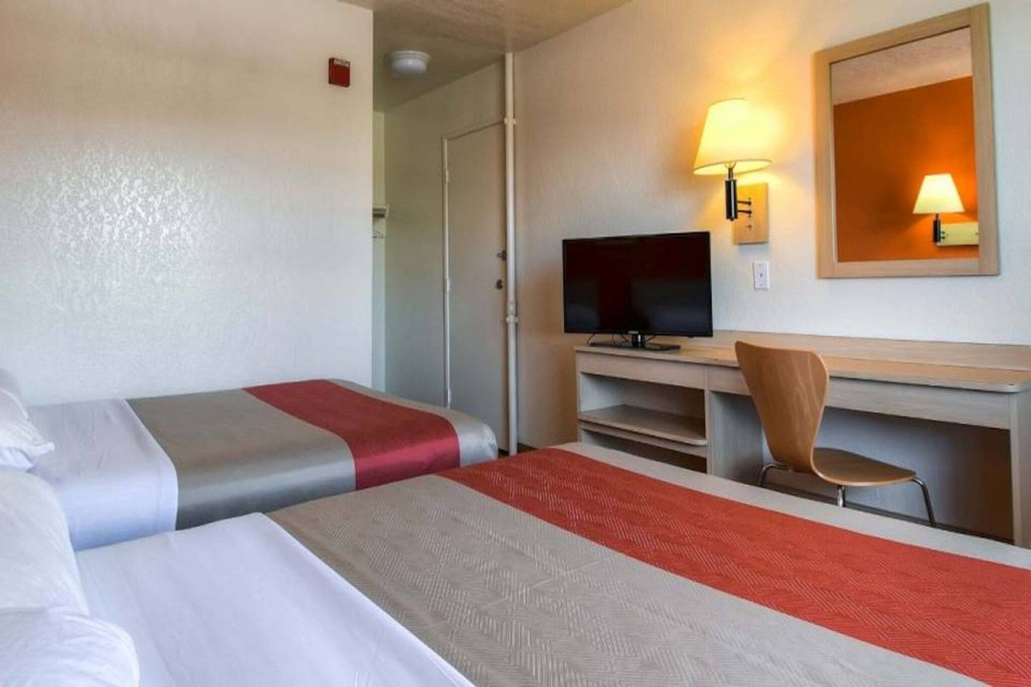 A hotel room with two beds, a television, a desk with a chair, and two wall-mounted lamps.
