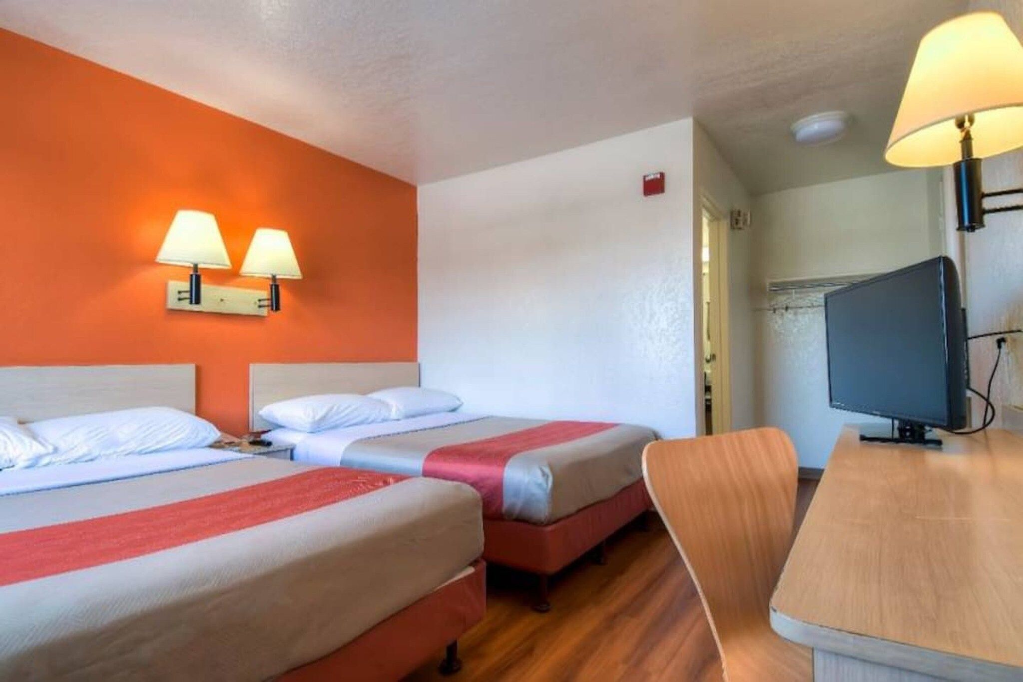 A hotel room with two beds, a desk, a television, and two wall-mounted lamps.