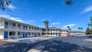 Un motel con varias habitaciones, un estacionamiento y un cielo azul despejado.