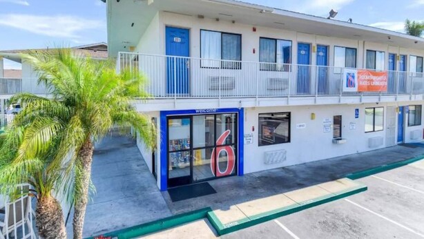 Un motel con entrada azul, un balcón con barandillas y una palmera en primer plano.