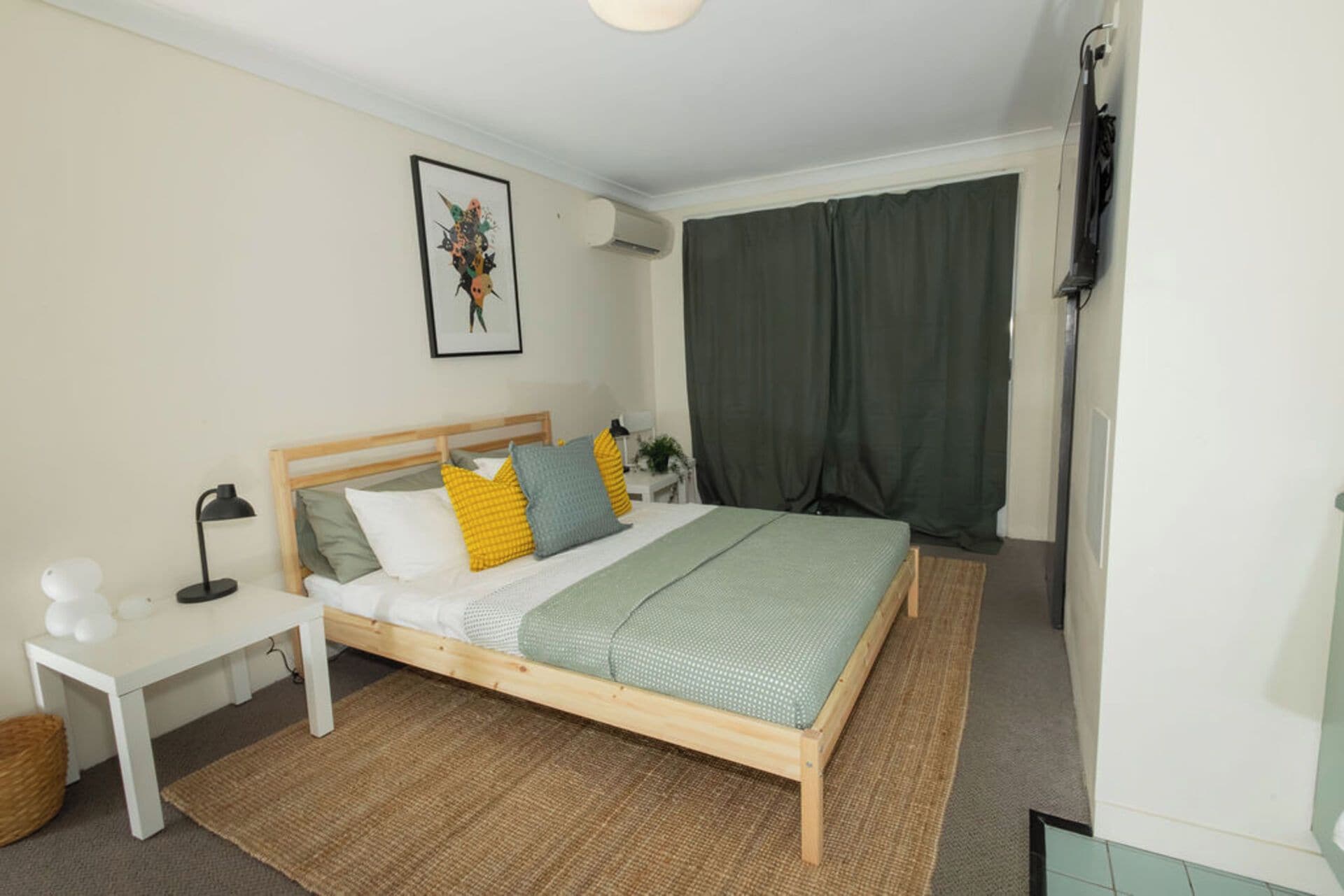 Un dormitorio con cama, mesita de noche, lámpara y un cuadro en la pared.
