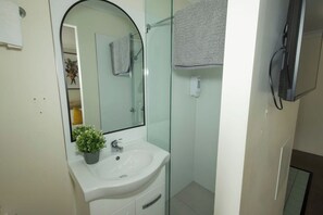 A bathroom with a white sink, a glass shower enclosure, and a mirror with a towel hanging on the wall. - Peaceful 1BD Studio with Balcony, Chermside (Chermside)
