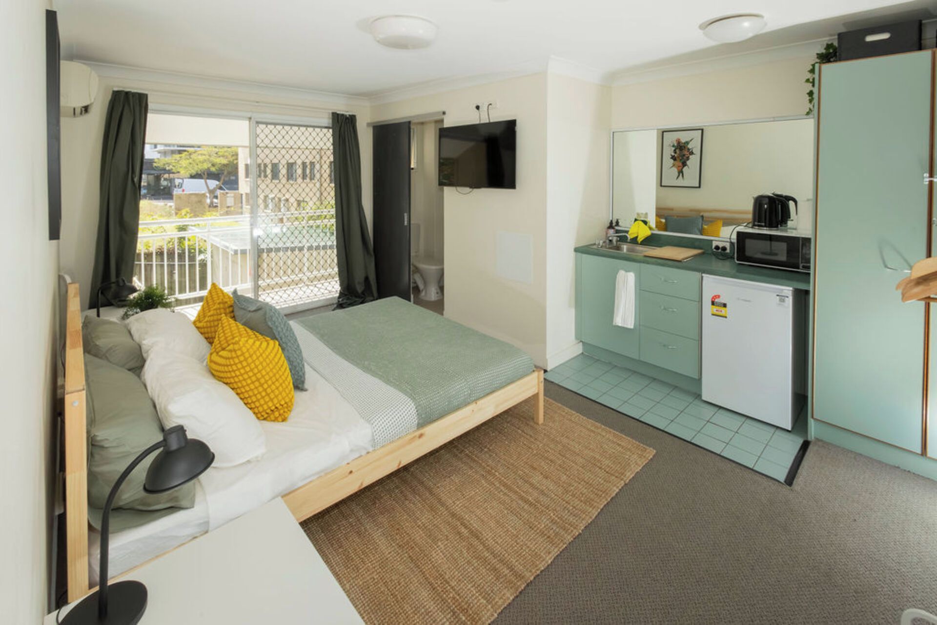 A compact bedroom with a bed, bedside table, and a view of the outside.
