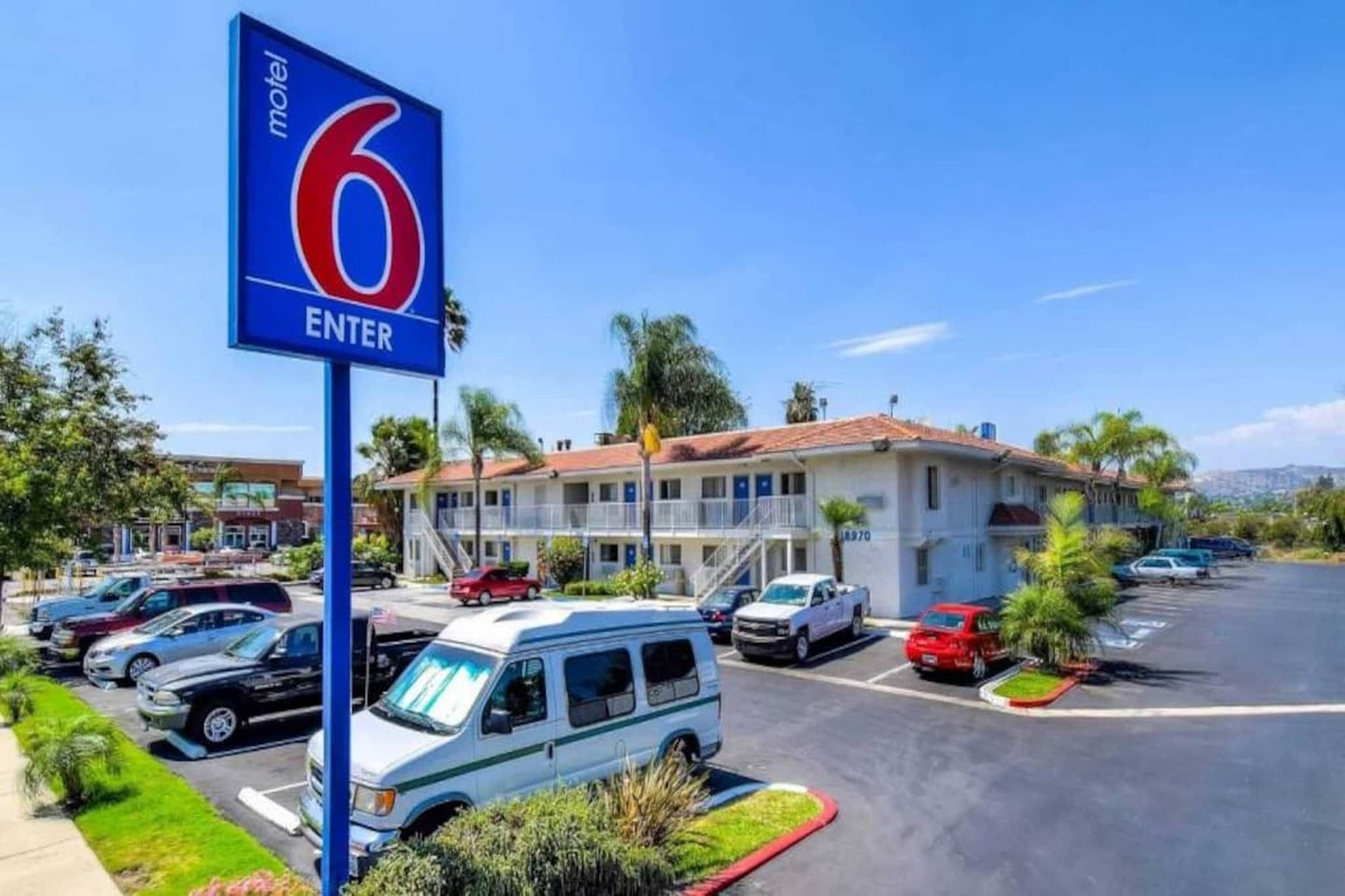 Ein Motel mit einem gut sichtbaren Schild '6 ENTER', einem Parkplatz mit verschiedenen Fahrzeugen und einem Gebäude mit rotem Dach.