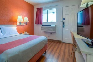 Ein Hotelzimmer mit einem Bett, Nachttischlampen, einem Schreibtisch, einem Stuhl, einem Fernseher, einer Klimaanlage und einem Fenster mit Vorhängen.