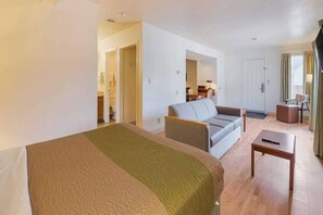 A hotel room with a bed, a sofa, a small table, and a separate seating area with a chair and a table. - 1 Queen Bed | ADA/RI Shower/Non-Smoking (Greensboro)
