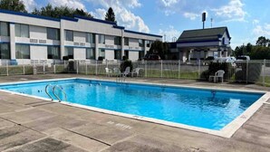 Ein Schwimmbecken mit einem 'NO DIVING'-Schild, umgeben von einem eingezäunten Bereich mit Liegestühlen und einem Gebäude im Hintergrund.