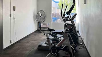 A gym with stationary bikes, a fan, and a window with a view of greenery.