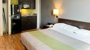 A hotel room with a bed, a nightstand, a lamp, a microwave, and a refrigerator. - 1 King Bed | Non-Smoking, Kitchen (Clarion)