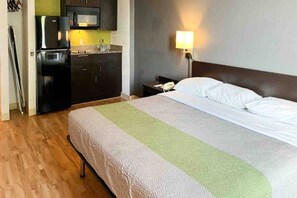 Een hotelkamer met een bed, nachtkastje, lamp, magnetron en koelkast.