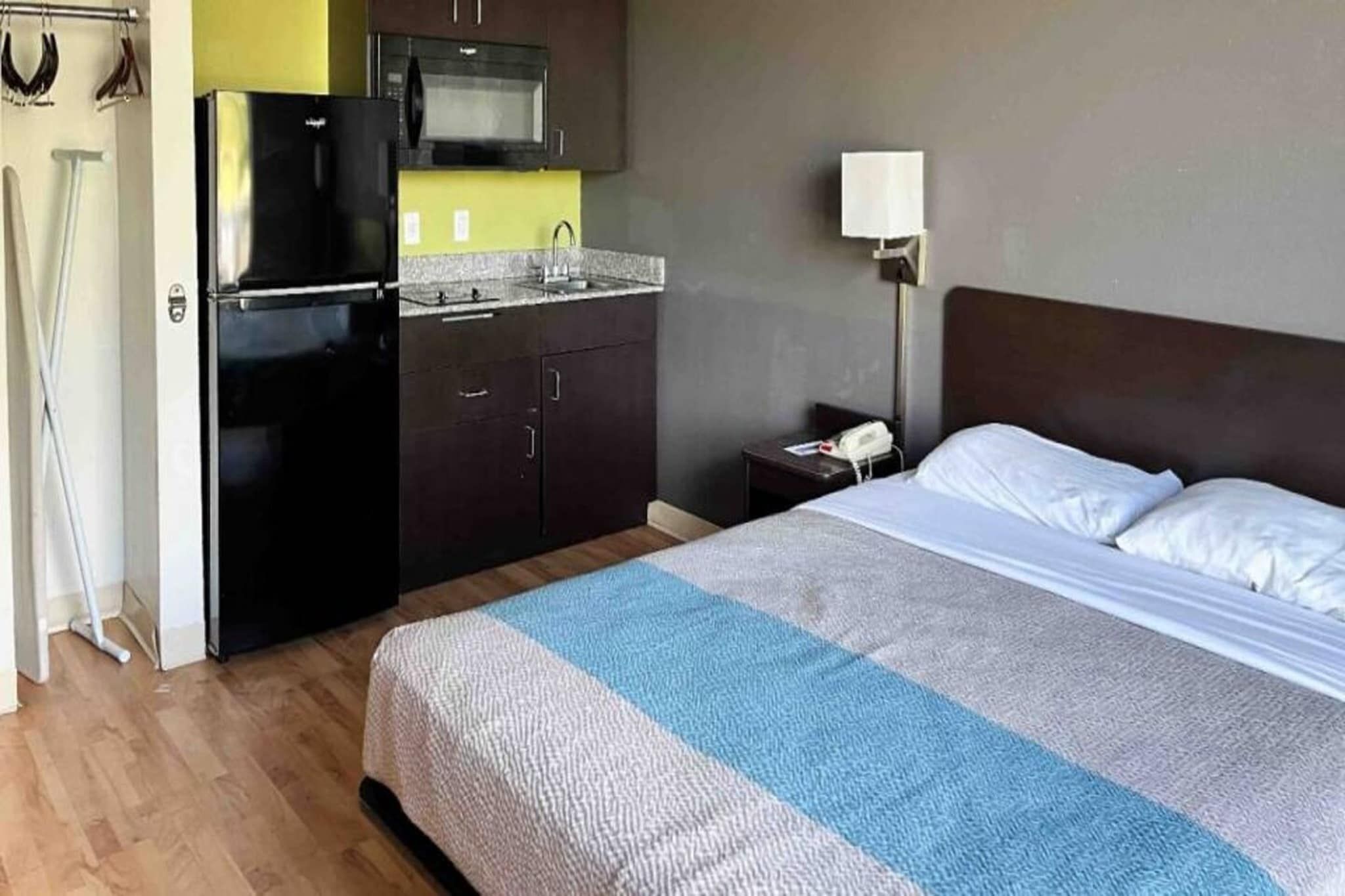 A hotel room with a bed, a nightstand, a lamp, a microwave, and a refrigerator.