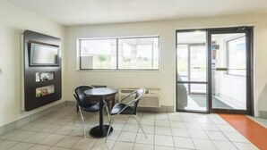 Una habitación con suelo de baldosas, una mesa con sillas, un televisor de pantalla plana en la pared y un amplio ventanal con vistas al exterior.
