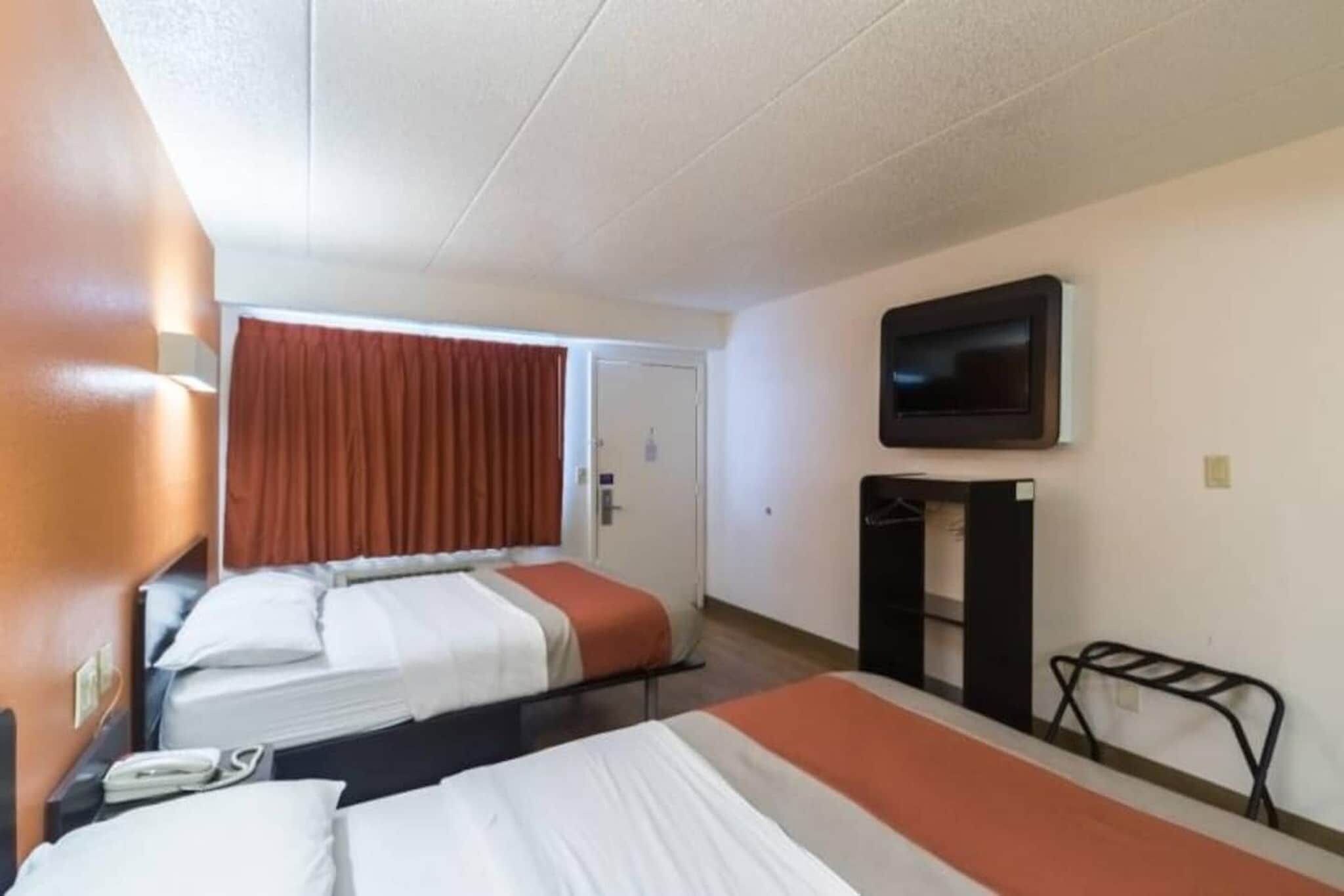 Quarto de hotel com duas camas, televisão, uma mesinha e uma porta.