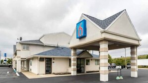 Un motel con un letrero que dice '6', un área de estacionamiento techada y un edificio de una sola planta.