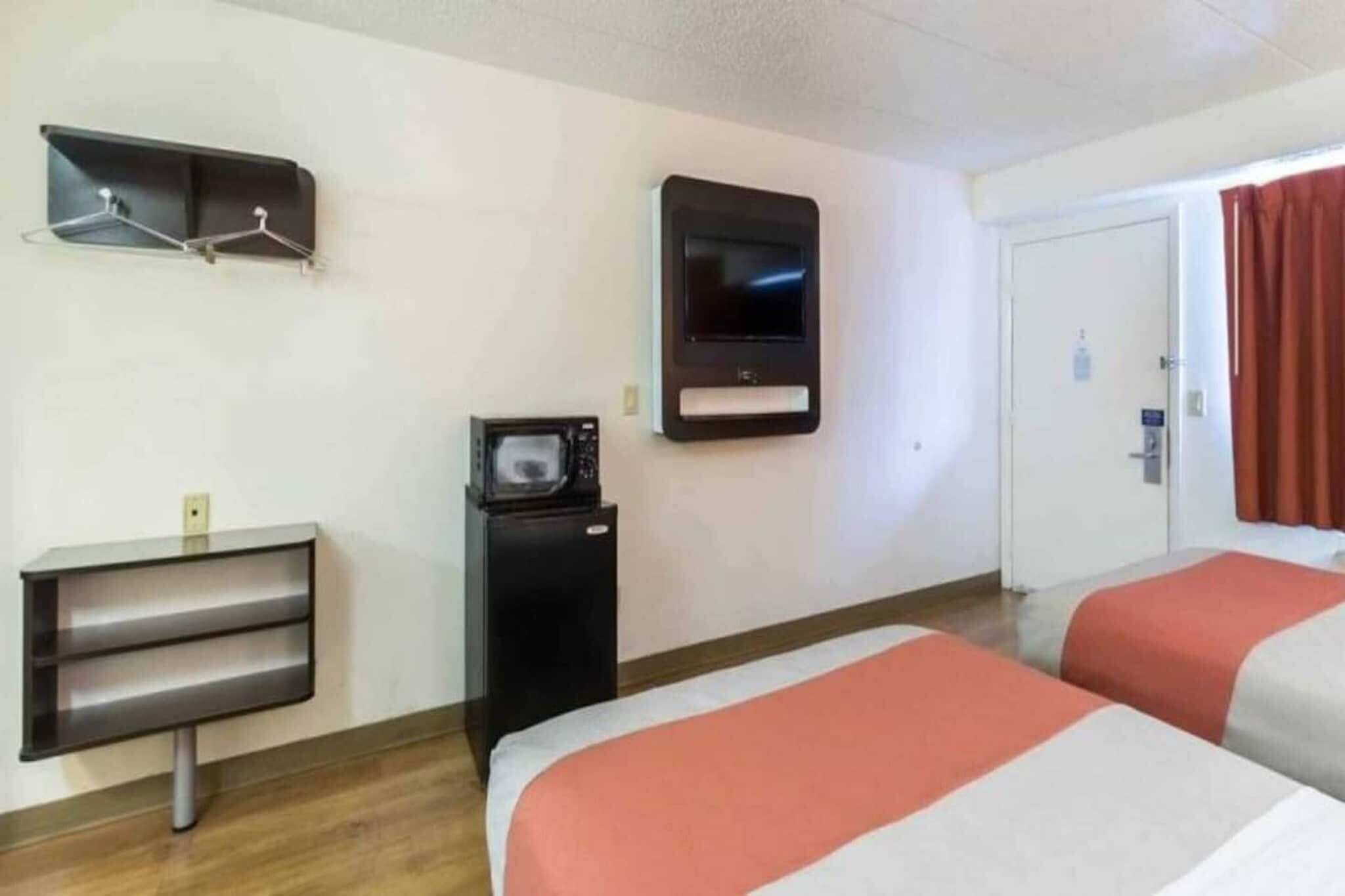 A hotel room with two beds, a TV, a small desk with a mirror, and a coat rack.