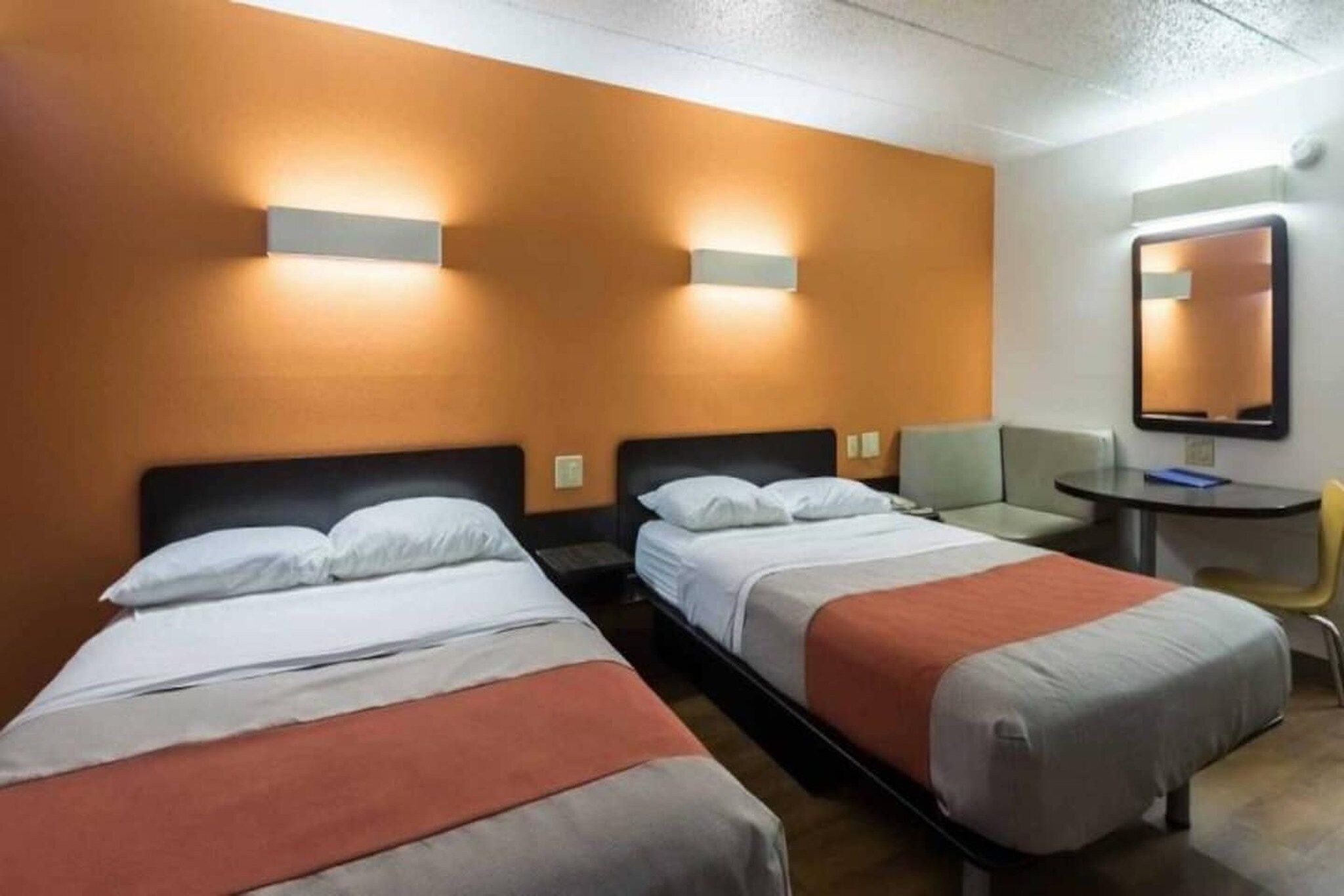 A hotel room with two single beds, a small table, a chair, and a mirror on the wall.