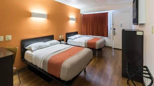 Habitación de hotel con dos camas, un escritorio, una silla y un televisor.
