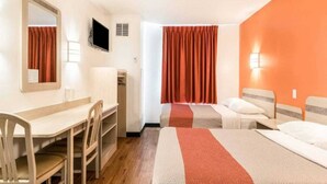 Ett hotellrum med ett skrivbord, två sängar, en tv och ett fönster med gardiner.