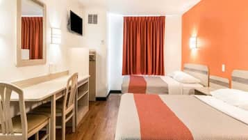 A hotel room with a desk, two beds, a television, and a window with curtains.