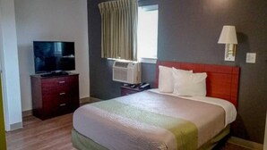 Una habitación de hotel con cama, televisión, aire acondicionado y lámpara.